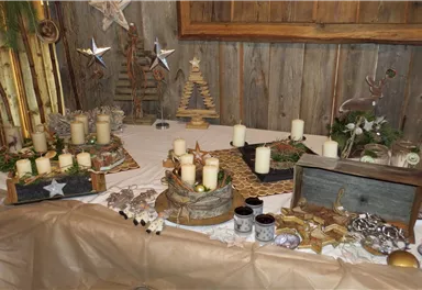 A festive table decoration with candles, stars, and pine branches. The rustic background creates a cozy atmosphere.