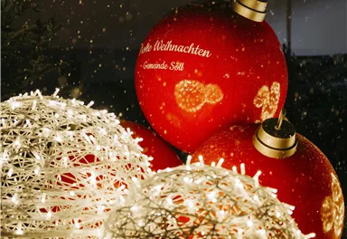 A festive Christmas decoration with red Christmas balls and bright, decorative orbs. In the background, dark windows can be seen, creating a cozy atmosphere.