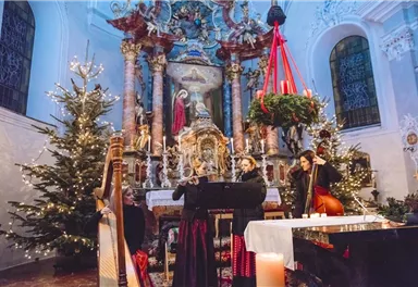 A festively decorated church with a Christmas tree and lights. Musicians are playing live in front of a traditional altar.
