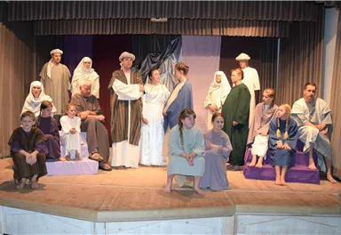 A group of people in historical costumes is standing on a stage. They seem to be part of a theater play or a performance.