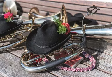 A collection of wind instruments on a wooden surface. Some instruments are wearing black hats with flowers and decorations.