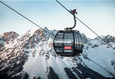 Eine Seilbahn schwebt über schneebedeckte Berge. Der Himmel ist klar und die Landschaft wirkt majestätisch.