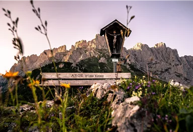 Ein schöner Berg mit einer Holzskulptur und bunten Blumen im Vordergrund. Die majestätischen Felsen sind in der Hintergrundsicht sichtbar.