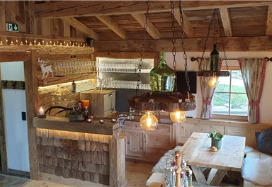 A cozy wooden cabin with a modern kitchenette and an inviting dining table. Soft lighting and rustic details create a warm atmosphere.