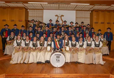 A group of musicians stands on a stage in traditional attire. They are surrounded by musical instruments and proudly present their ensemble.