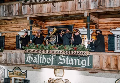 A brass band is playing on a wooden balcony. The name "Gashof Stangl" is clearly visible.