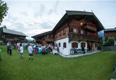 A traditional alpine hut with a beautiful garden. Many people are gathered outside for a festive occasion.