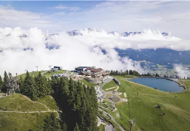 Eine schöne Berglandschaft mit Nebel und einem klaren See. Im Hintergrund sind ein Restaurant und Wanderwege zu sehen.