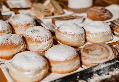 Ein Teller mit verschiedenen Gebäckstücken, darunter zuckerbestäubte Hefekränze und Zimtrollen. Die süßen Teilchen sind frisch und einladend angerichtet.