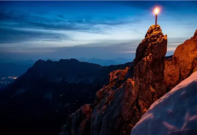 An impressive mountain horizon at twilight, illuminated by a candle on a high rock. The scene conveys a calm and mystical atmosphere.