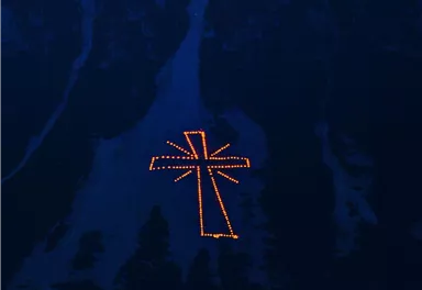 A large, glowing cross in the darkness. It is visible on a mountain or in a landscape.