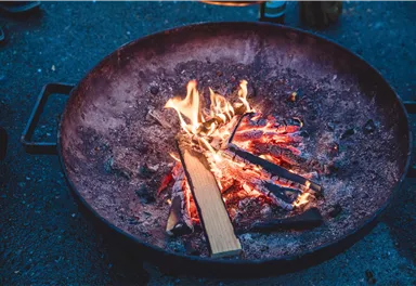 An open fire in a large metal pan, surrounded by glowing coals. The flames flicker and create a cozy atmosphere.