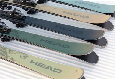 Eine Reihe von Skiern liegt nebeneinander. Die Skier haben verschiedene Farbtöne und sind mit dem Markennamen "HEAD" gekennzeichnet.