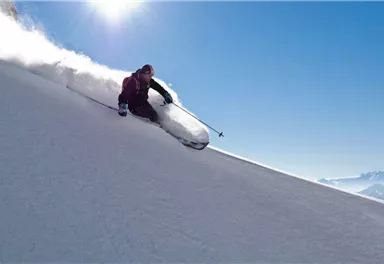 Ein Skifahrer fährt über eine schneeweiße Piste. Die Sonne strahlt am blauen Himmel und erzeugt eine schöne Winterlandschaft.