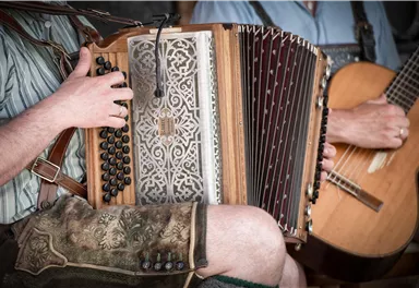 A musician plays an accordion while another musician holds a guitar. Both are wearing traditional clothing.