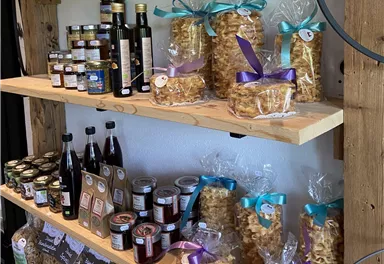 A wooden table with shelves full of food products. There are bottles, jams, and neatly packaged sweets with colorful ribbons.