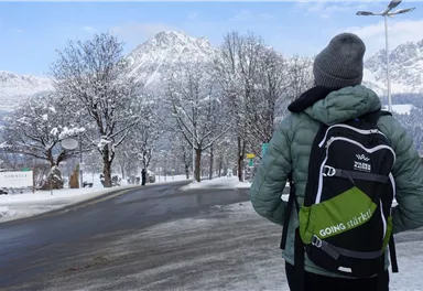 A person stands on a snow-covered road and looks at the mountains. Surrounded by snowy trees, the scene is calm and wintry.