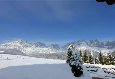 A snow-covered landscape with majestic mountains in the background. The sky is clear and bright blue.