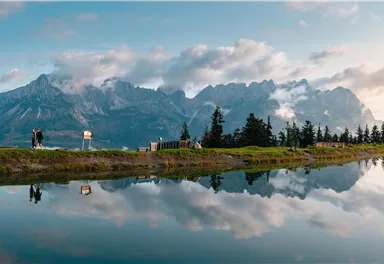 An impressive mountain landscape with reflective water in the foreground. The sky is partly cloudy and the view is very picturesque.