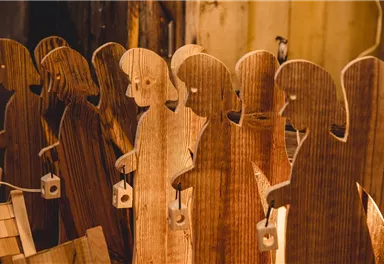 A group of wooden figures stands in a row. Each figure holds a small birdcage in its hand.