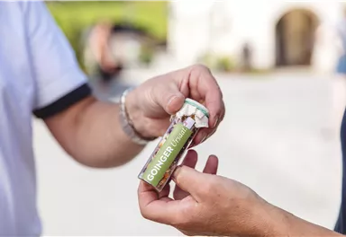 A farmer stands in a field and inspects the plants. In the background, trees and gentle hills can be seen.