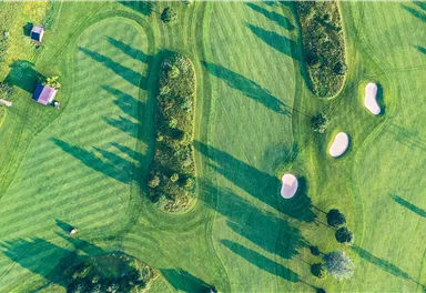 Eine stilvolle Golfanlage mit gepflegtem Grün und Sandbunkern. Lange Schatten fallen von den Bäumen auf das Fairway.