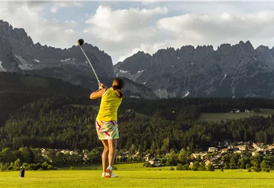 Eine person spielt Golf auf einem schönen Platz, umgeben von Bergen. Der Himmel ist teilweise bewölkt und die Landschaft ist grün und gepflegt.