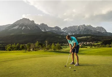 Ein Golfer puttet auf einem grünen Platz mit malerischen Bergen im Hintergrund. Die Landschaft ist ruhig und idyllisch.