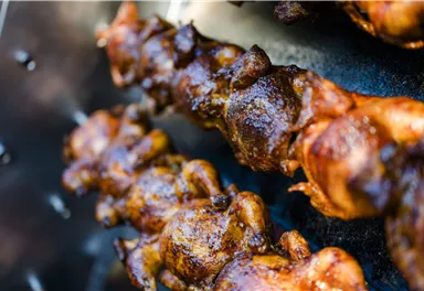 A delicious skewer with grilled chicken that looks golden brown and crispy. The background features a grill area with more pieces of chicken.