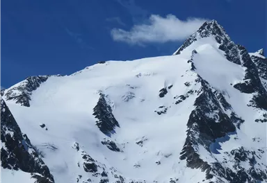 A majestic mountain with snow-capped peaks under a clear blue sky. The landscape radiates coldness and beauty.