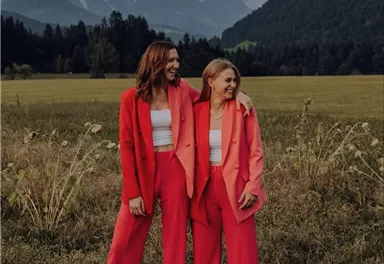 Ein Musiker spielt akustische Gitarre und singt in einem Freiluftbereich. Im Hintergrund sind Menschen und eine schöne Landschaft zu sehen.