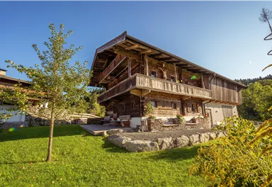 A cozy wooden house with several balconies and a large garden. The sun is shining and the sky is clear.