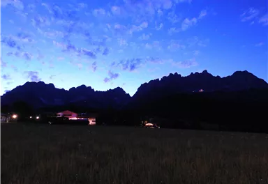 Eine atemberaubende Berglandschaft bei Dämmerung, mit einer schimmernden Silhouette der Berge. Der Himmel ist klar und in sanften Blau- und Violetttönen gefärbt.