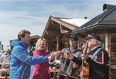 Eine Gruppe von Freunden stößt mit Biergläsern an. Sie sitzen an einem Tisch und genießen die gemeinsame Zeit in einer gemütlichen Umgebung.