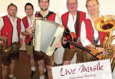 A group of four musicians in traditional costumes stands on stage. They play different instruments and promote a live music event at the Hexenalm hotel.