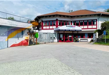 Ein modernes Gebäude mit dem Schriftzug "Kaiserbad". Es gibt bunte Wandmalereien und eine einladende Eingangstür.