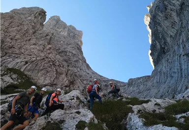 Eine Gruppe von Kletterern erklimmt felsige Gipfel in einer beeindruckenden Berglandschaft. Der Himmel ist klar und das Terrain ist steinig mit wenig Vegetation.