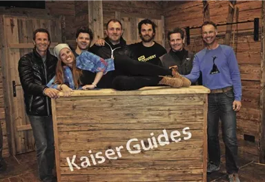 A group of seven people is smiling at a wooden counter. The surroundings have a rustic, cozy charm.