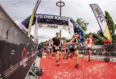 Läufer überqueren die Ziellinie bei einem Wettkampf in den Bergen. Die Atmosphäre ist festlich und die Teilnehmer strahlen Freude aus.