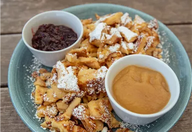 A plate with delicious waffles, sprinkled with powdered sugar. There are also two bowls with chocolate sauce and applesauce.