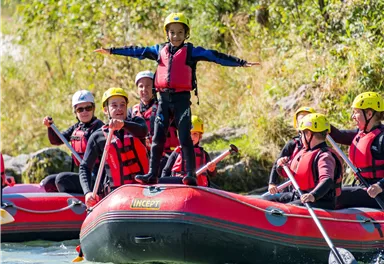 A group of people in an inflatable boat on a clear river. A child stands with outstretched arms at the front of the boat.