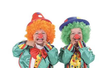Zwei fröhliche Kinder als Clowns, mit bunter Kleidung und lustigen Perücken. Sie lächeln und zeigen mit den Händen auf ihre roten Nasen.
