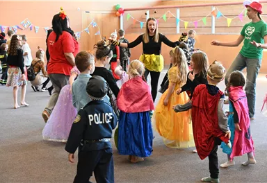 Eine lebhafte Kinderparty mit verkleideten Kindern, die Freude haben. In der Mitte tanzen und spielen sie zusammen.
