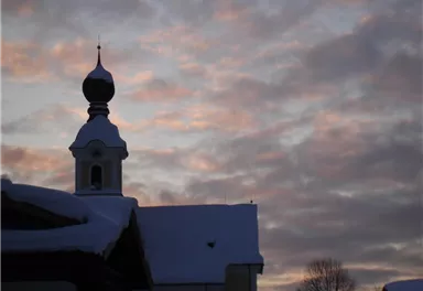 A snow-covered building against a colorful sky at sunset. The silhouette with a distinctive dome appears picturesque and peaceful.