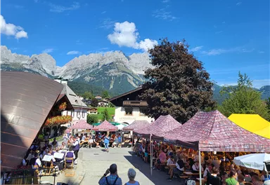 A lively festival with many tents and visitors in a picturesque mountain landscape. The sky is clear and the surroundings are surrounded by nature.