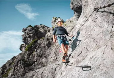 A climber is on a rocky wall. He uses safety equipment to move up securely.