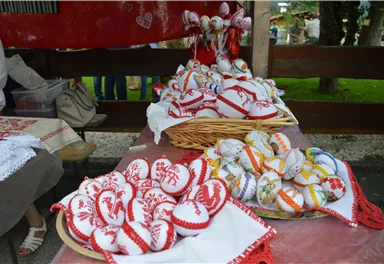 Beautiful, handcrafted heart ornaments lie on a table. The colorful designs feature traditional patterns and are arranged in baskets and on fabrics.