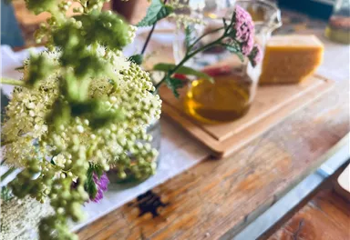 A tray with olive oil and cheese is on a wooden table. Fresh flowers are visible in the foreground.