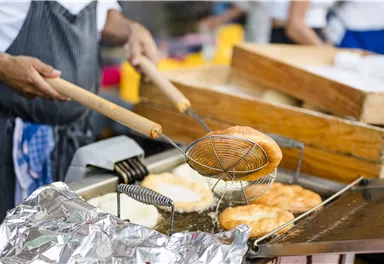 A cook is frying fresh pasta in a hot oil pan. In the background, other ingredients and utensils can be seen.