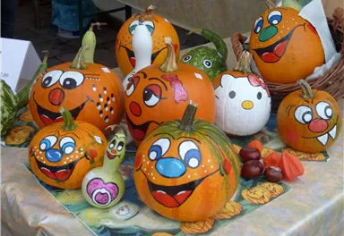 Eine Gruppe von bunten, bemalten Kürbissen mit fröhlichen Gesichtern. Die Kürbisse stehen auf einem Tisch und sind mit verschiedenen Charakteren dekoriert.